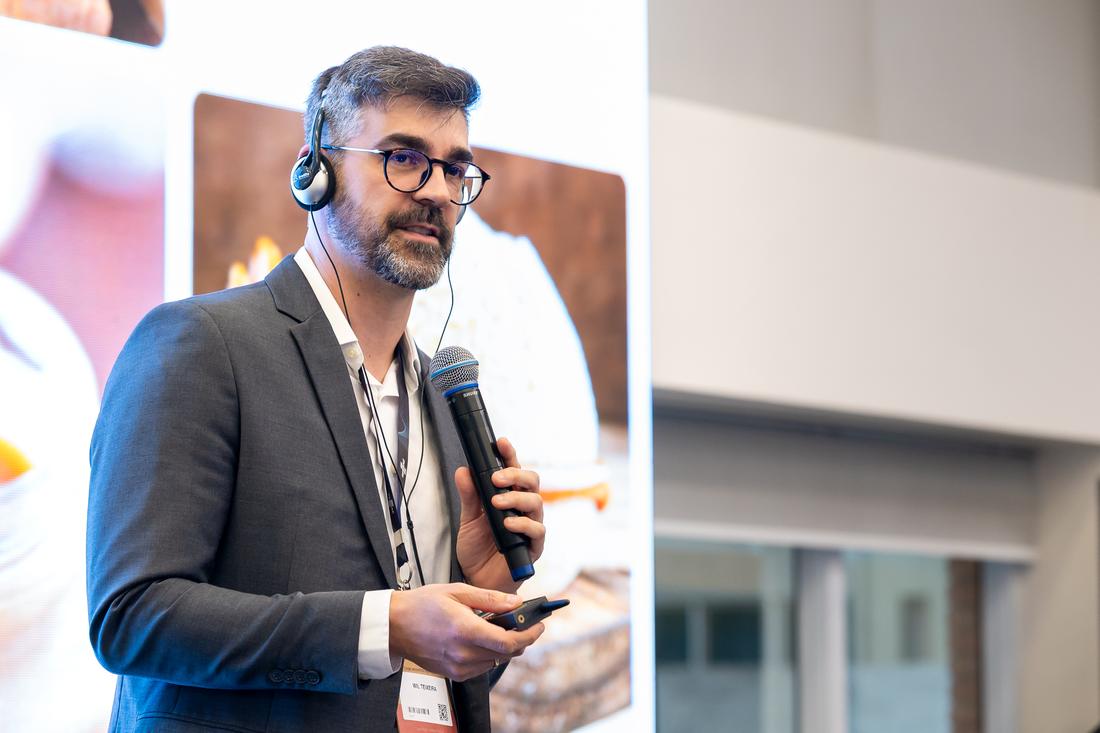 Wil Teixeira falando ao microfone em um palco